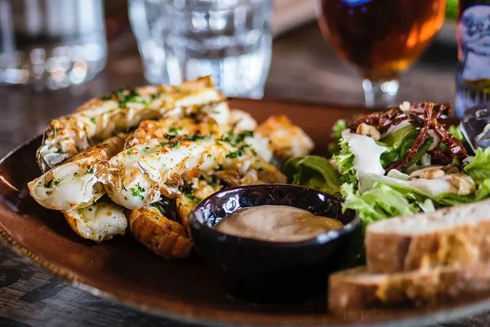 A plate featuring grilled shrimp with herbs, a side salad, dipping sauce, and slices of bread.
